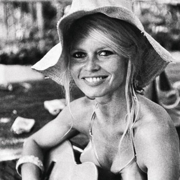Brigitte Bardot mit Hut und Gitarre lächelt.