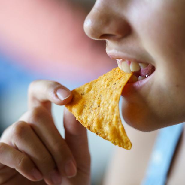 Unrecognizable happy teenage girl biting spicy nacho chip at home