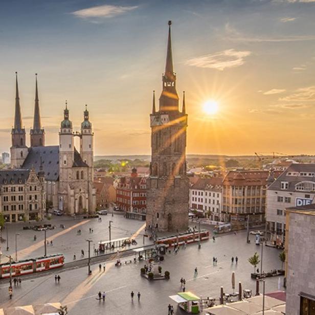 Sonnenuntergang über einem Stadtplatz mit markanten Türmen im Hintergrund.