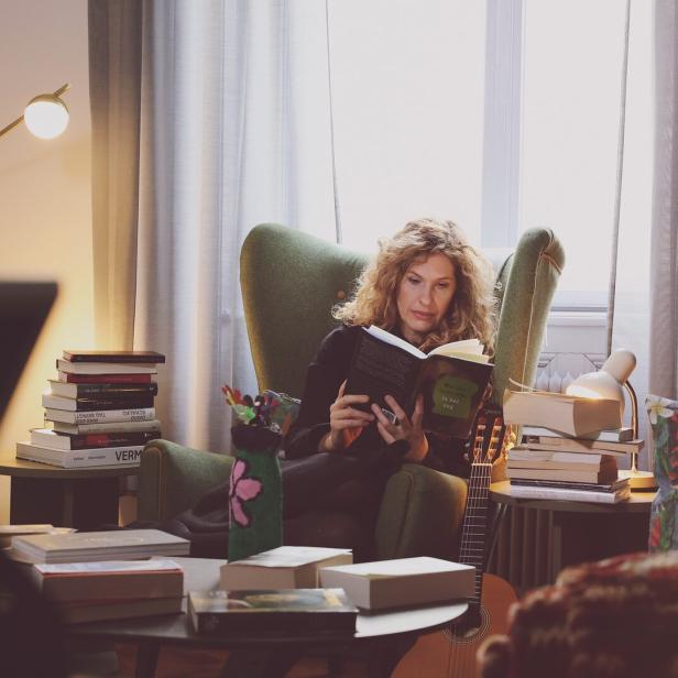 Lotte de Beer beim Lesen in einem Sessel - vor ihr türmen sich Bücher.