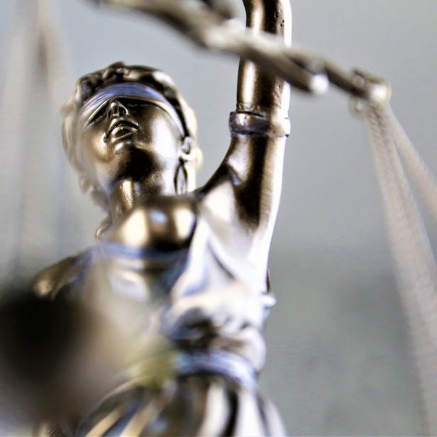 Eine silberne Justitia-Figur mit verbundenen Augen hält eine Waage in der erhobenen Hand.