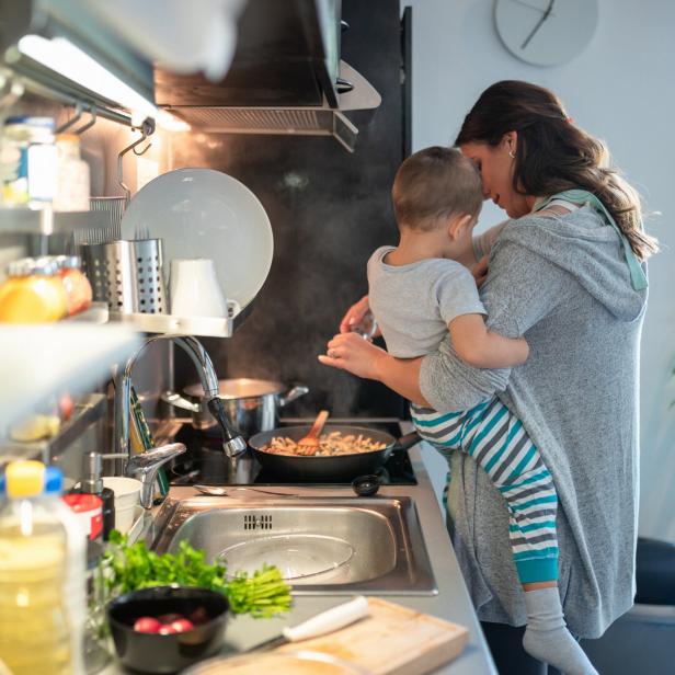 Mother carrying toddler on hip and preparing meal