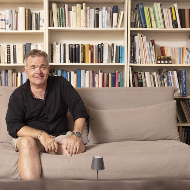 Cornelius Obonya sitzt lässig auf einer Couch vor seinem Bücherregal.