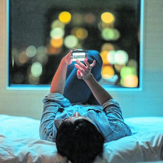 Woman lying down on bed and using smart phone at night