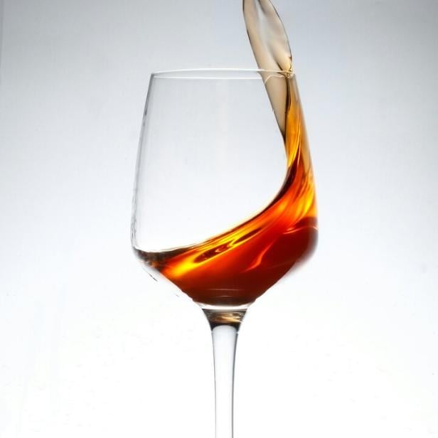 Ein Weinglas steht auf einer nassen Oberfläche und eine braune Flüssigkeit schwappt heraus