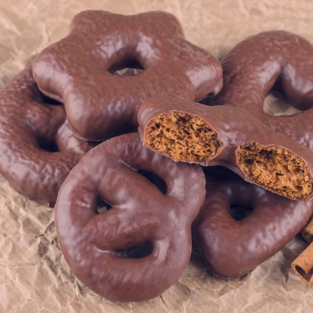 Mehrere mit Schokolade überzogene Lebkuchen in verschiedenen Formen liegen auf braunem Papier, daneben Zimtstangen und Sternanis.