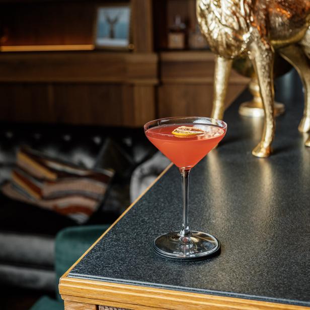 Romy Cocktail, in einer dunklen Bar auf einem Tisch ein Orangener Cocktail in einem edlen Glas