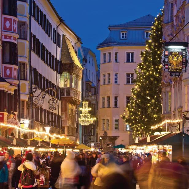 Ein belebter Weihnachtsmarkt in Innsbruck mit geschmücktem Baum und dem Gasthof Goldener Adler im Hintergrund.