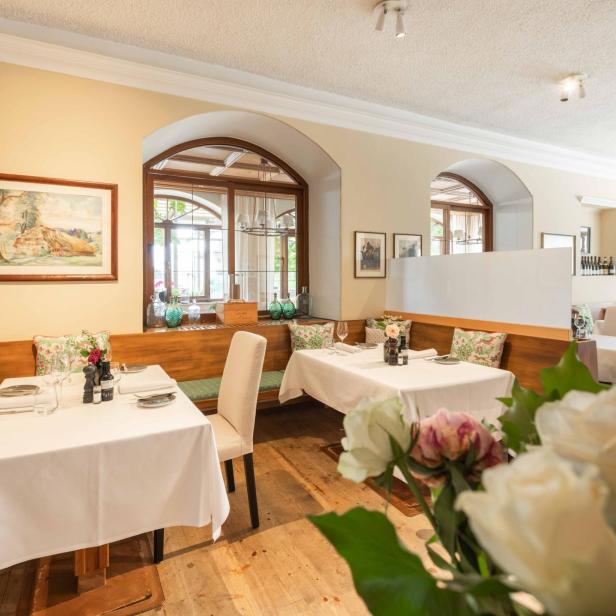 Der einladende Gastraum des Lokals "Das Bräu" mit gedeckten Tischen, Holzbänken und floralen Kissen unter hellen Wänden.