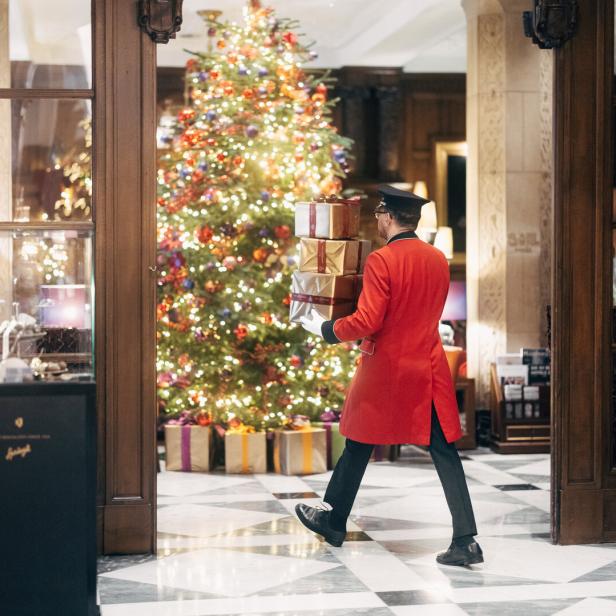 Ein Mann, der ein Geschenk in eine Hotellobby mit einem großen Christbaum trägt.