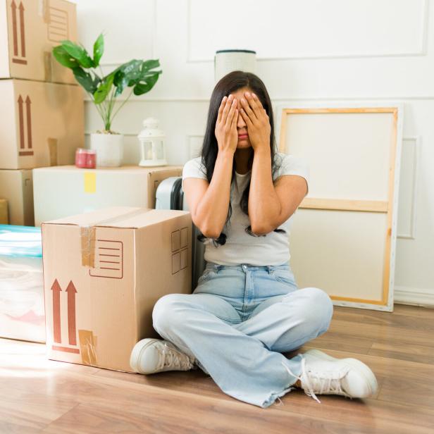 Eine Frau sitzt auf dem Boden zwischen Umzugskartons und bedeckt ihr Gesicht mit den Händen.