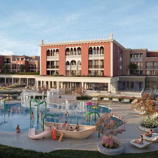 Vor einem großen, venezianisch wirkenden Gebäude entspannen Menschen auf Liegen und spielen Kinder in einem Pool mit Wasserspielen und Rutsche.