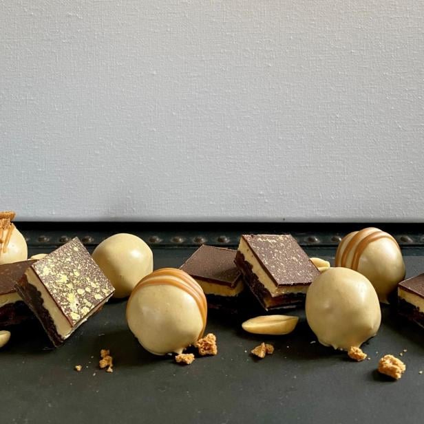 Mehrere Pralinen und Schokoladenstücke mit goldenen Verzierungen und Erdnüssen liegen auf einer dunklen Oberfläche.