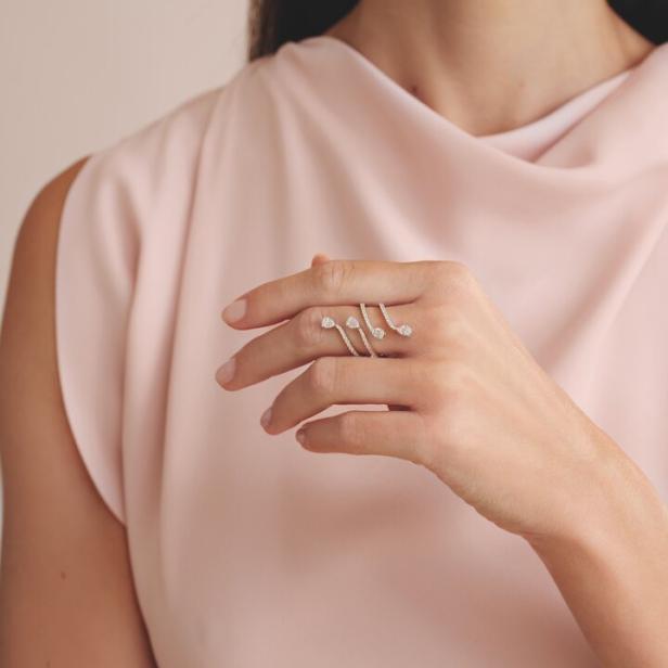 Eine Frau im rosa Kleid mit einem silbernen Ring am Finger, den sie in die Kamera hält