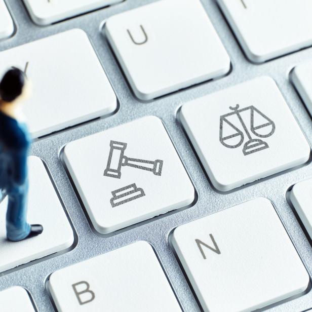 Eine kleine Figur steht auf einer Computertastatur mit Tasten, die Richterhammer und Waage zeigen.