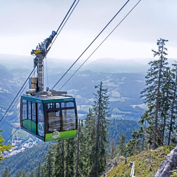 Eine grüne Rax-Seilbahn schwebt vor einer Berglandschaft.