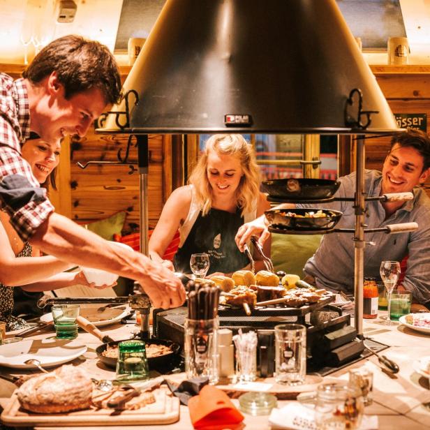 Menschen grillen gemeinsam an einem Tisch in eine Holzhütte.