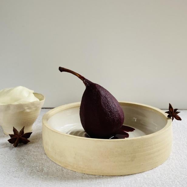 Eine pochierte Birne in einer Schale, garniert mit Sternanis, neben einem Schälchen Creme.