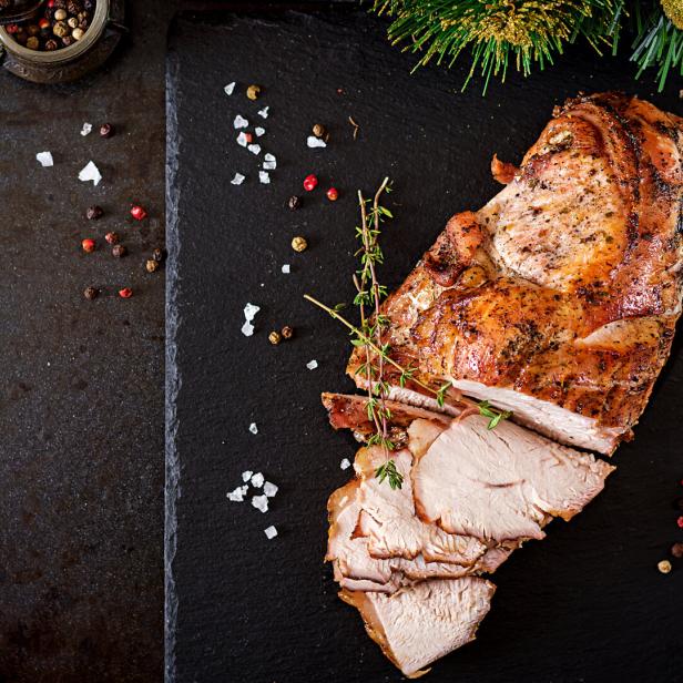 Roasted sliced Christmas ham of turkey on dark rustic background. Top view. Festival food.