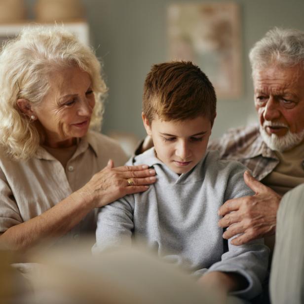 Ein Junge sitzt traurig zwischen seinen tröstenden Großeltern auf einer Couch