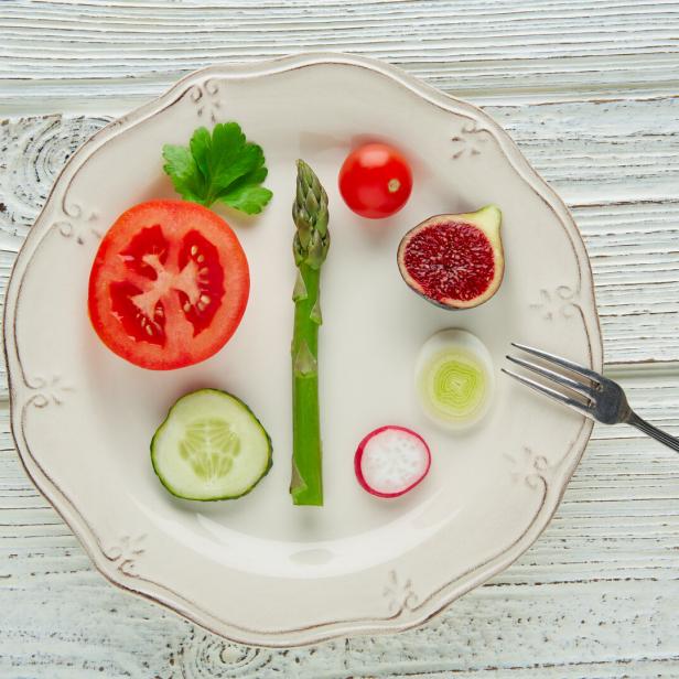 Verschiedene Gemüsescheiben, eine Feige und ein Spargel liegen dekorativ auf einem weißen Teller mit einer kleinen Gabel.
