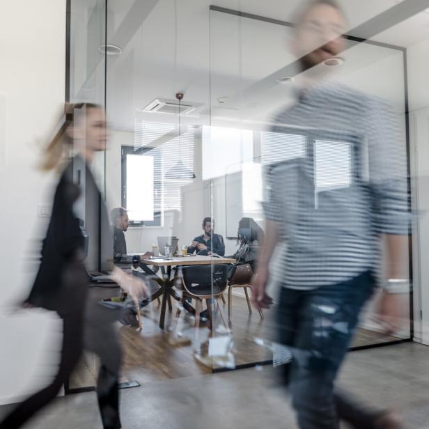 Im Büro gehen verschwommene Personen vorbei, während andere an einem Tisch sitzen.