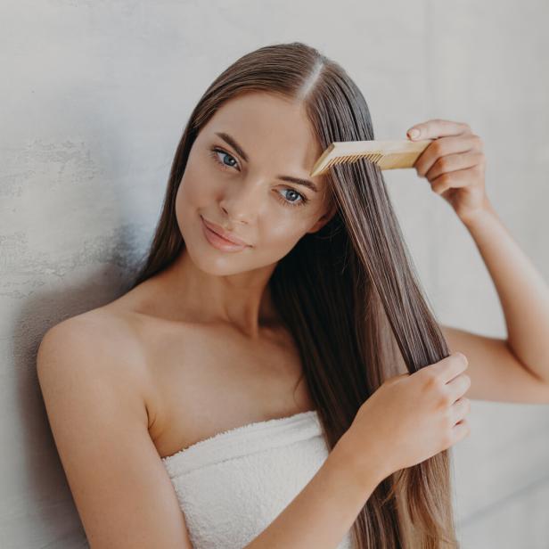 Eine junge Frau mit einem Handtuch um den Körper kämmt ihr langes, braunes Haar.