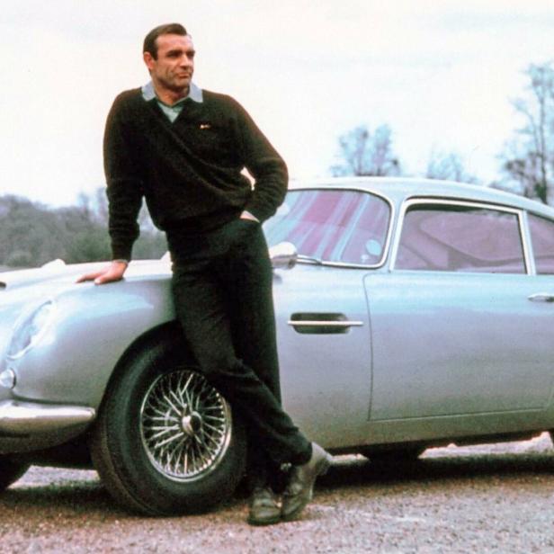 Sean Connery lehnt lässig an einem silbernen Aston Martin DB5 mit dem Kennzeichen BMT 216A.