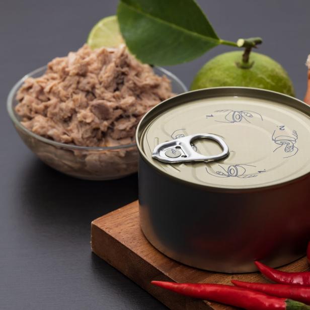 Eine ungeöffnete Konservendose steht neben einer Schale mit Thunfisch, Limette, Schalotten, Tomaten und roten Chilischoten.