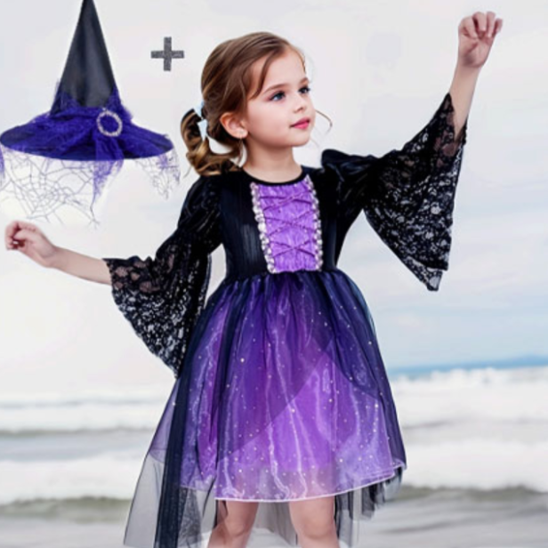 Mädchen im lila-schwarzen Hexenkostüm mit passendem Hexenhut am Strand.