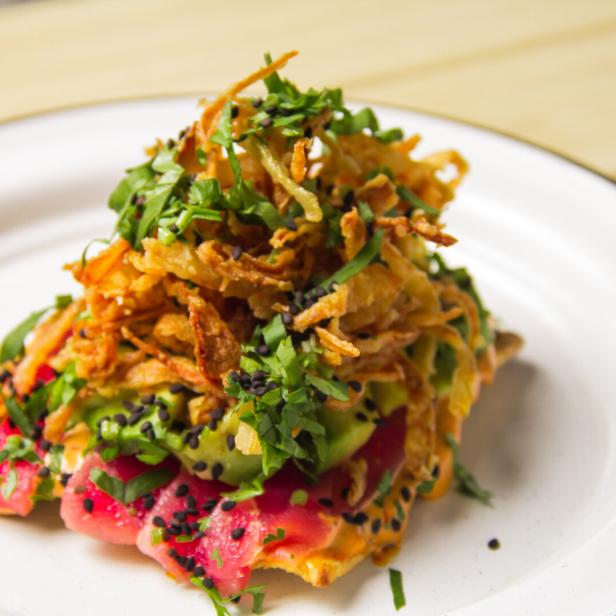 Auf einem Teller liegt ein Gericht mit Thunfisch, Avocado, frittierten Zwiebeln und Kräutern.