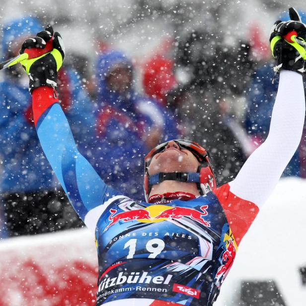 Ein Skirennläufer mit Startnummer 19 jubelt mit erhobenen Armen im Schneefall, im Hintergrund Zuschauer.
