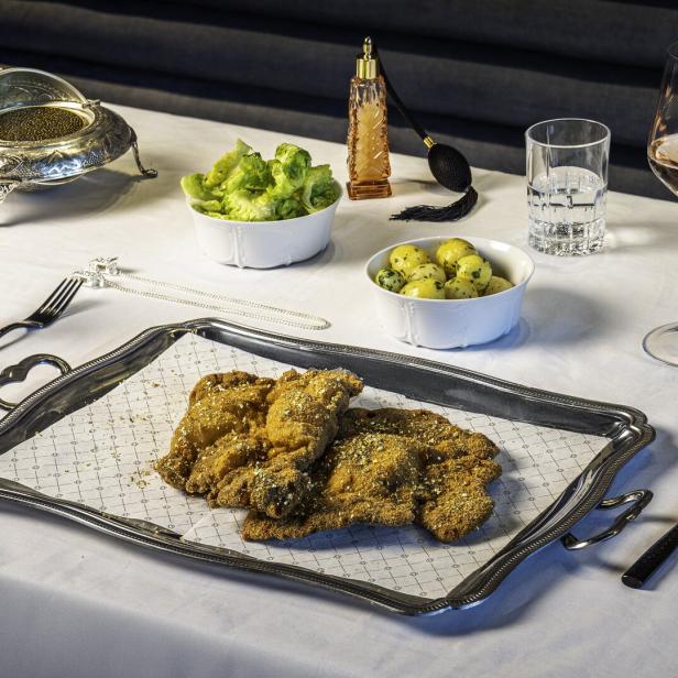 Auf einem gedeckten Tisch stehen Schnitzel auf einem Serviertablett, dazu Salat, Kartoffeln, Kaviar und Getränke.