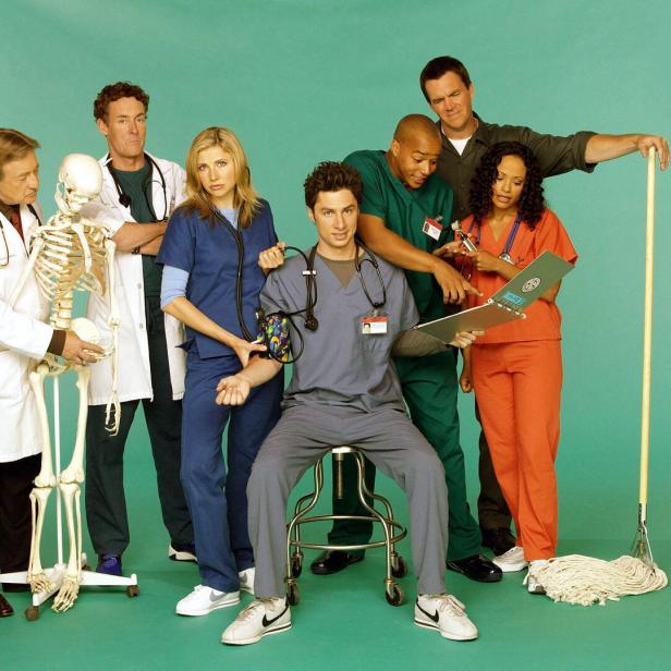 Sieben Personen in Krankenhauskleidung stehen zusammen, eine Person sitzt, ein Skelett und ein Wischmopp sind zu sehen.