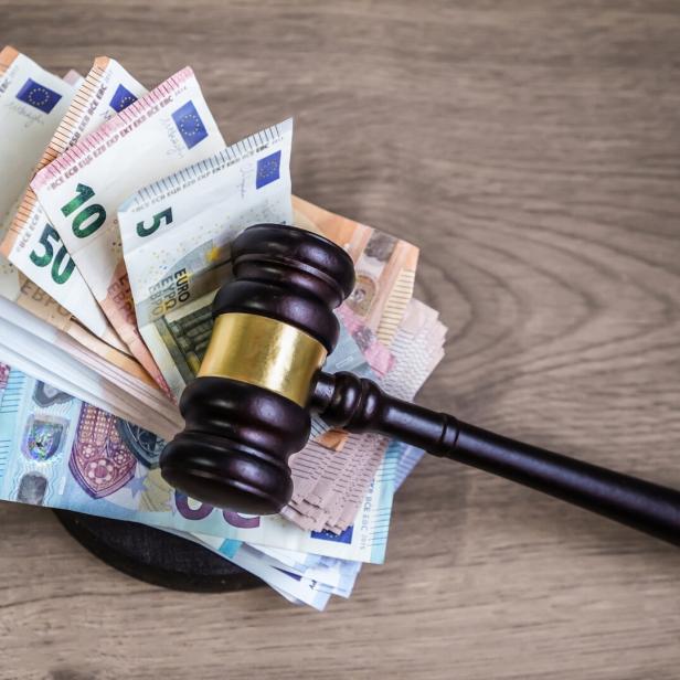 Ein Richterhammer liegt auf einem Stapel verschiedener Euro-Geldscheine auf einer Holzoberfläche.