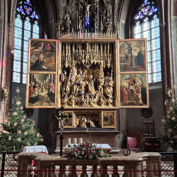 Ein Altar mit goldenem Altaraufsatz und Gemälden steht in einer Kirche mit Weihnachtsbäumen.