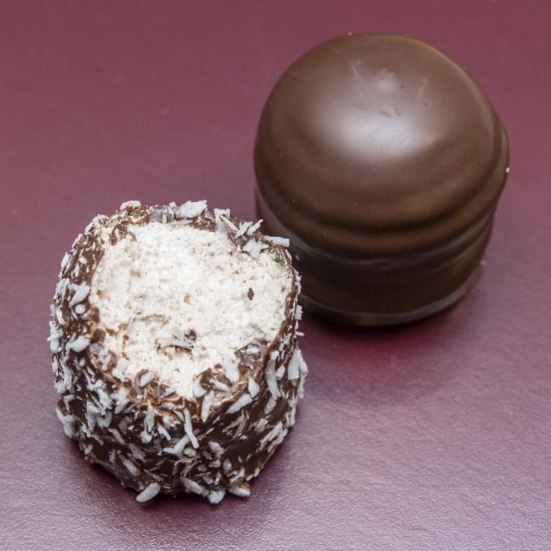 Zwei Schokoküsse, einer davon mit Kokosraspeln und angebissen, auf einer roten Oberfläche.