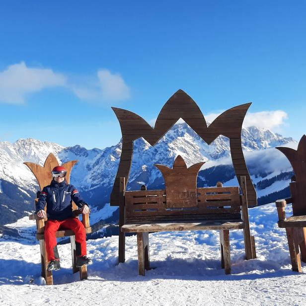 Ein Skifahrer sitzt auf einem Thron vor einer verschneiten Berglandschaft.