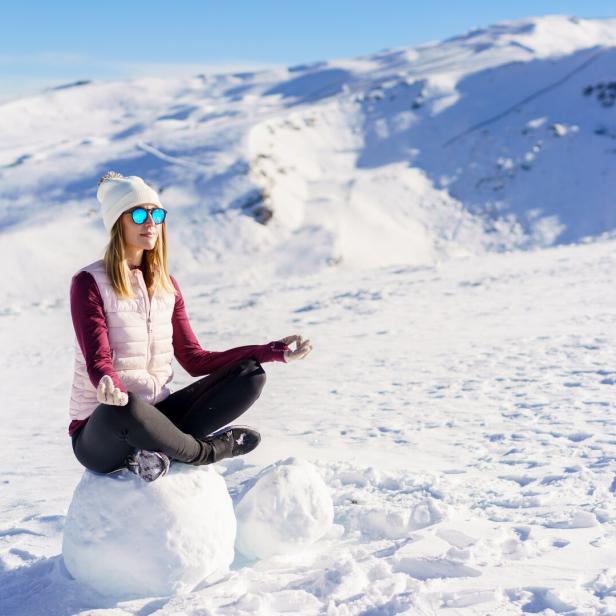 Cheerful woman sitting with lotus pose on snow