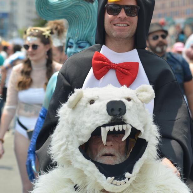 Mehrere Menschen in fantasievollen Kostümen, darunter ein Pinguin mit roter Fliege und ein Eisbärkostüm mit offenem Maul.