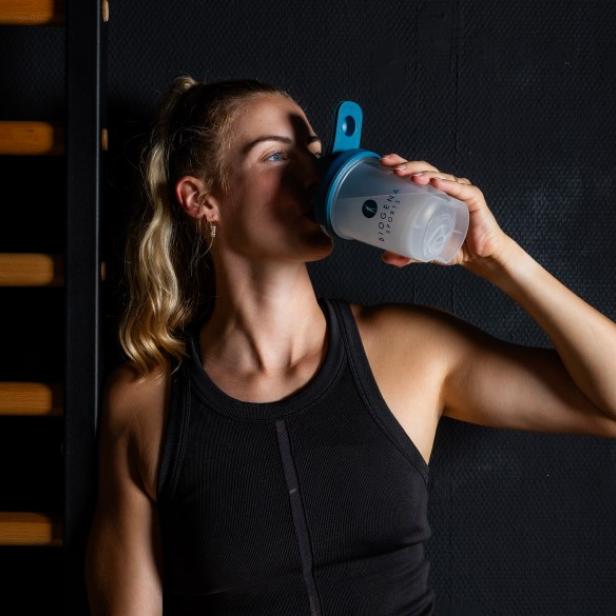 Eine Frau trinkt einen Proteinshake aus einer Trinkflasche.