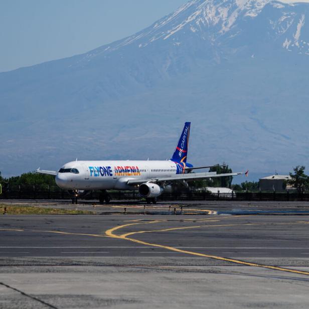 Ein Flugzeug von FlyOne Armenia steht vor einem schneebedeckten Berg auf einer Startbahn.