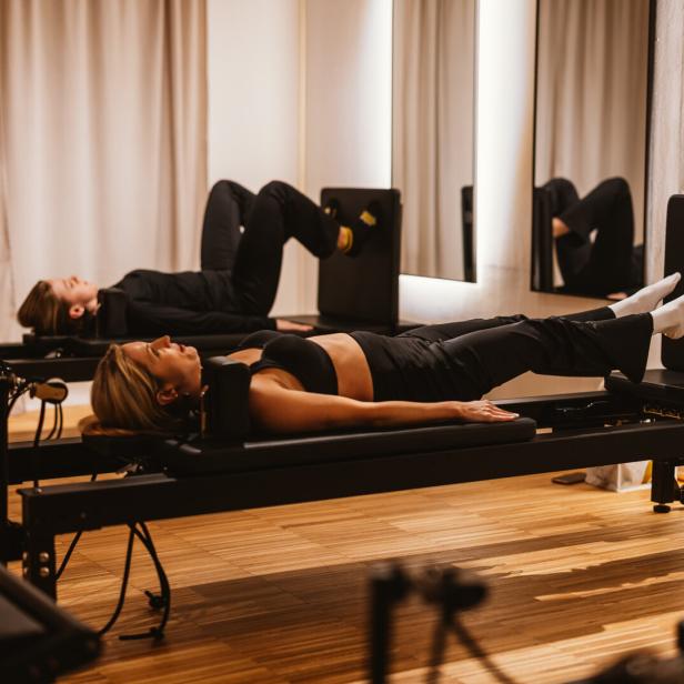 Zwei Frauen trainieren auf Pilates-Reformer-Jumpboard-Geräten in einem hellen Studio.