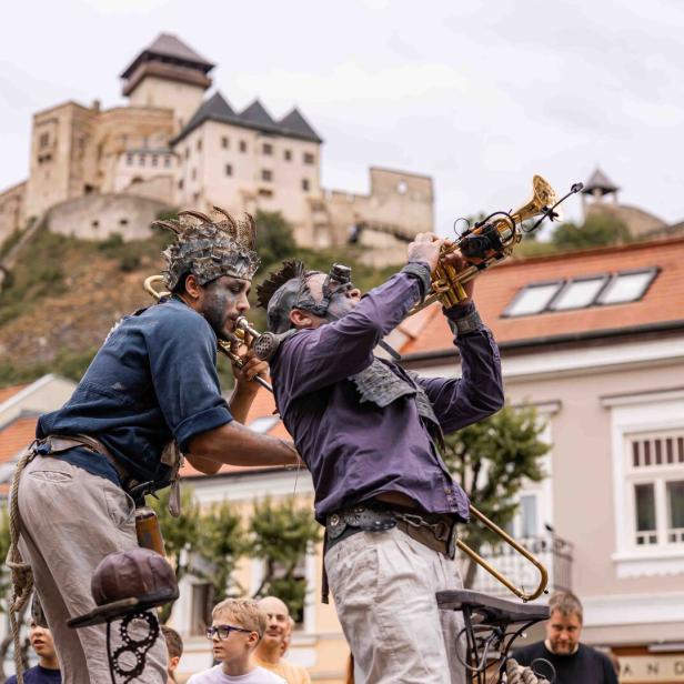 Zwei Musiker mit fantasievollen Kostümen spielen Trompete vor einer Burg und begeistern das Publikum.