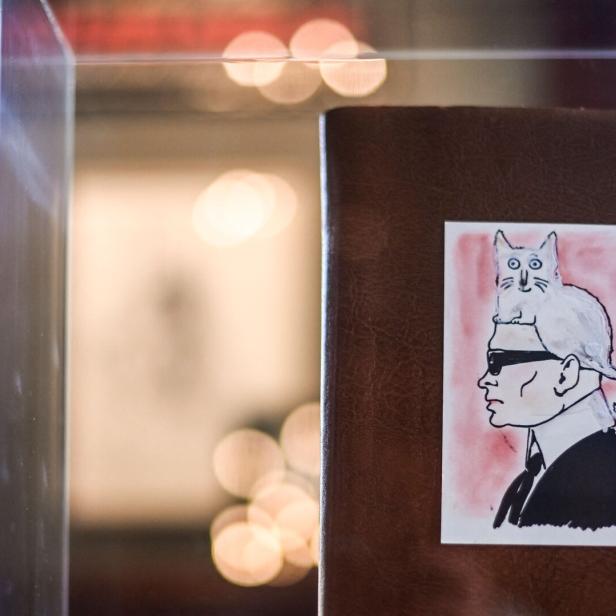 Ein Bild zeigt eine Zeichnung von Karl Lagerfeld mit seiner Katze Choupette auf dem Kopf.
