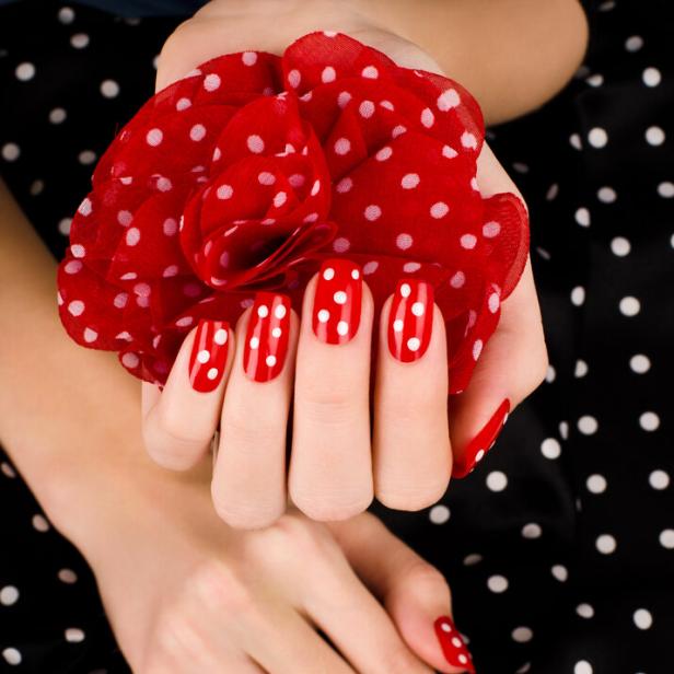 Rote Fingernägel mit weißen Punkten, dazu eine rote Stoffblume und schwarzer Stoff mit weißen Punkten.