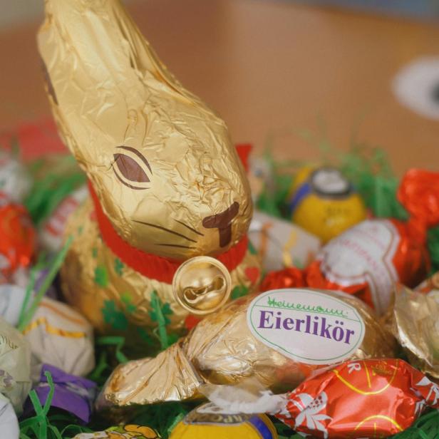 Ein goldener Lindt-Osterhase steht zwischen verschiedenen bunten Ostersüßigkeiten in einem Nest aus grünem Kunstgras.