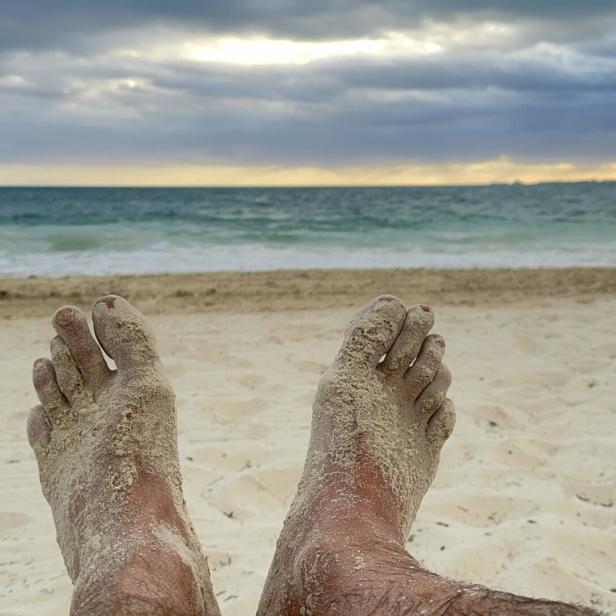 Sandige Füße entspannen am Strand mit Blick auf das Meer unter bewölktem Himmel.