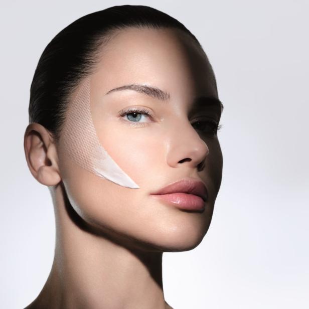 Frau mit glatter Haut und Creme auf der Wange, teilweise im Schatten.