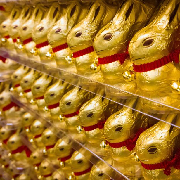 Viele goldene Schokoladenhasen mit roten Bändern und Glöckchen stehen dicht an dicht in Regalen.